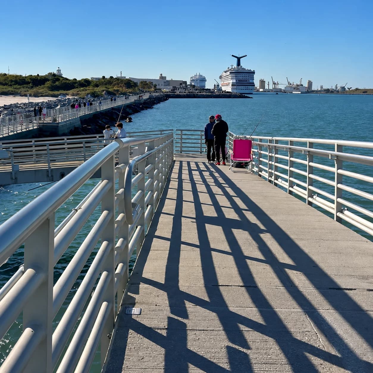 Jetty Park Pier's white-railed walkway with anglers and Port Canaveral ships beyond