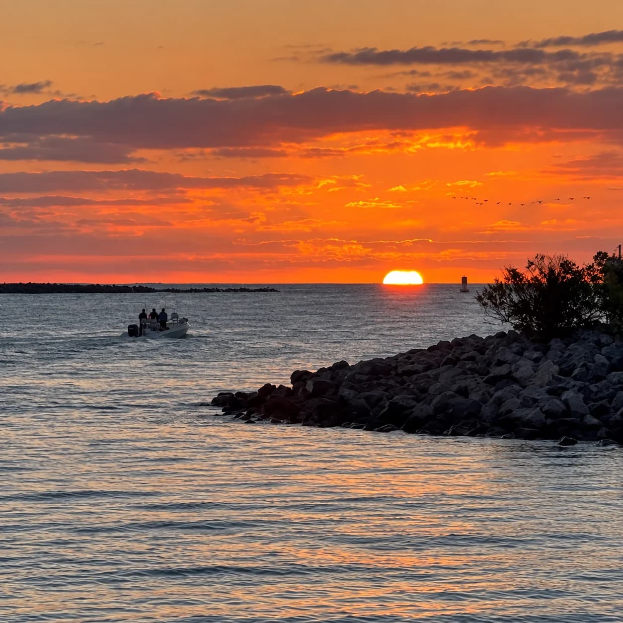 A small fishing boat heading through the Port Canaveral inlet at sunrise beside the rocky jetty